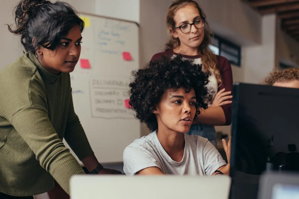 Quatre jeunes femmes travaillant autour d'un moniteur d'ordinateur 