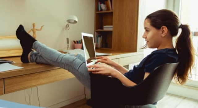 Jeune fille assise à son bureau avec ordinateur portable