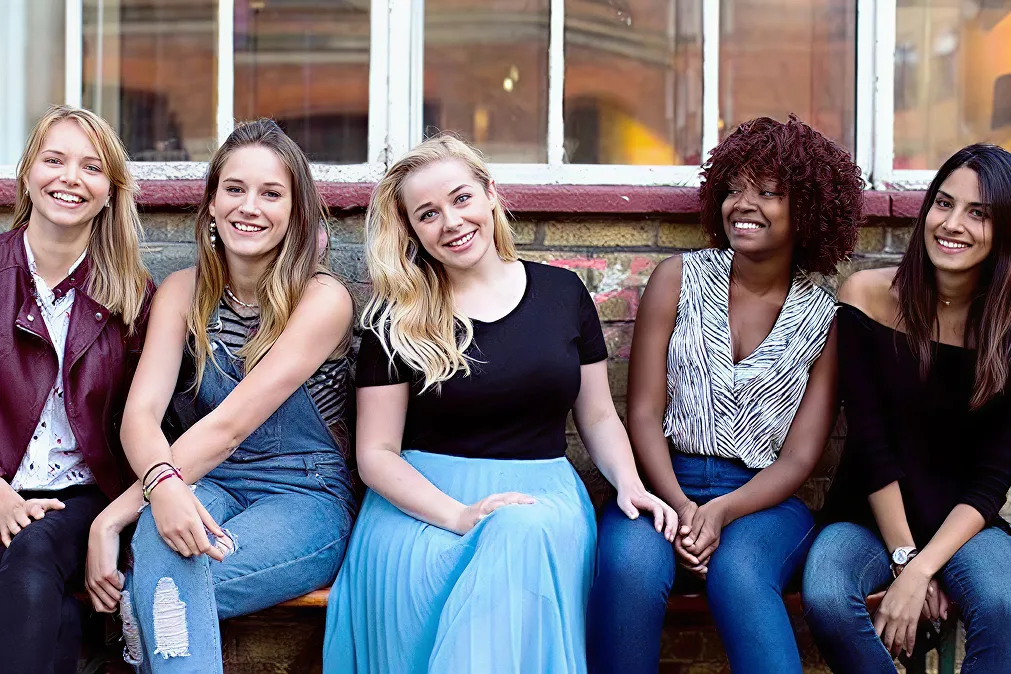 Cinq jeunes filles souriantes assises sur un banc