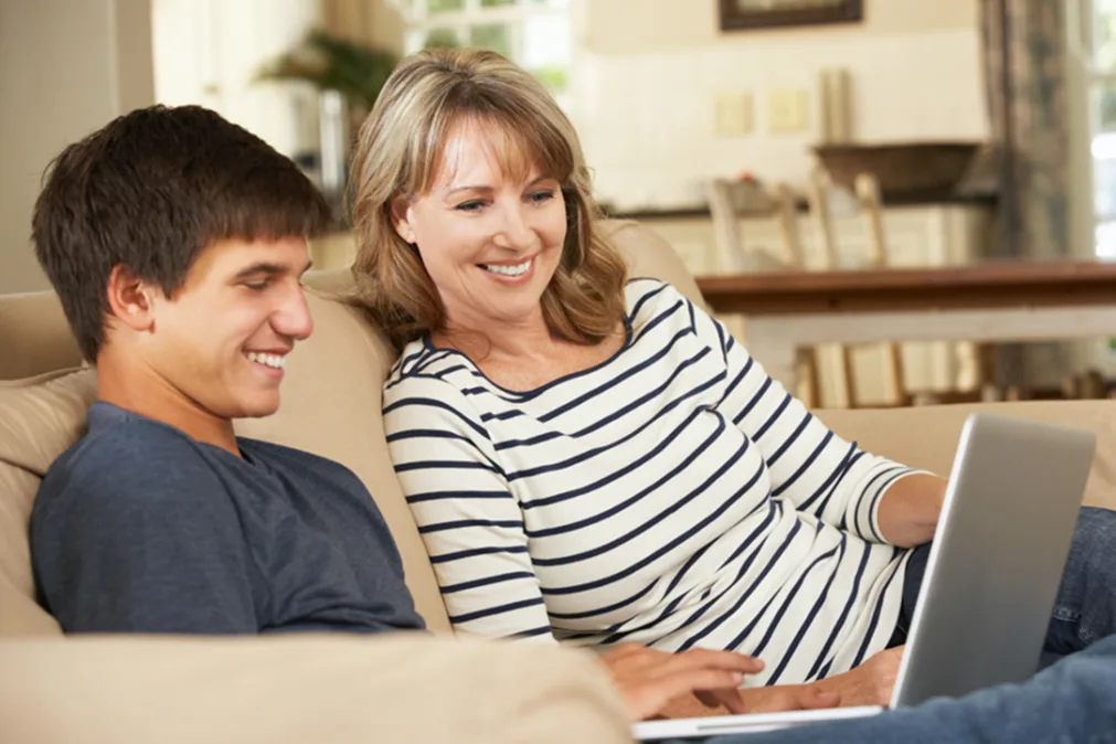 Maman et fils avec ordinateur portable sont assis sur un canapé