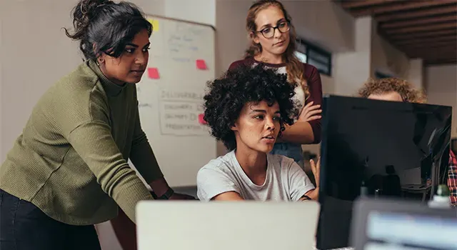 Quatre jeunes femmes travaillant autour d'un moniteur d'ordinateur 