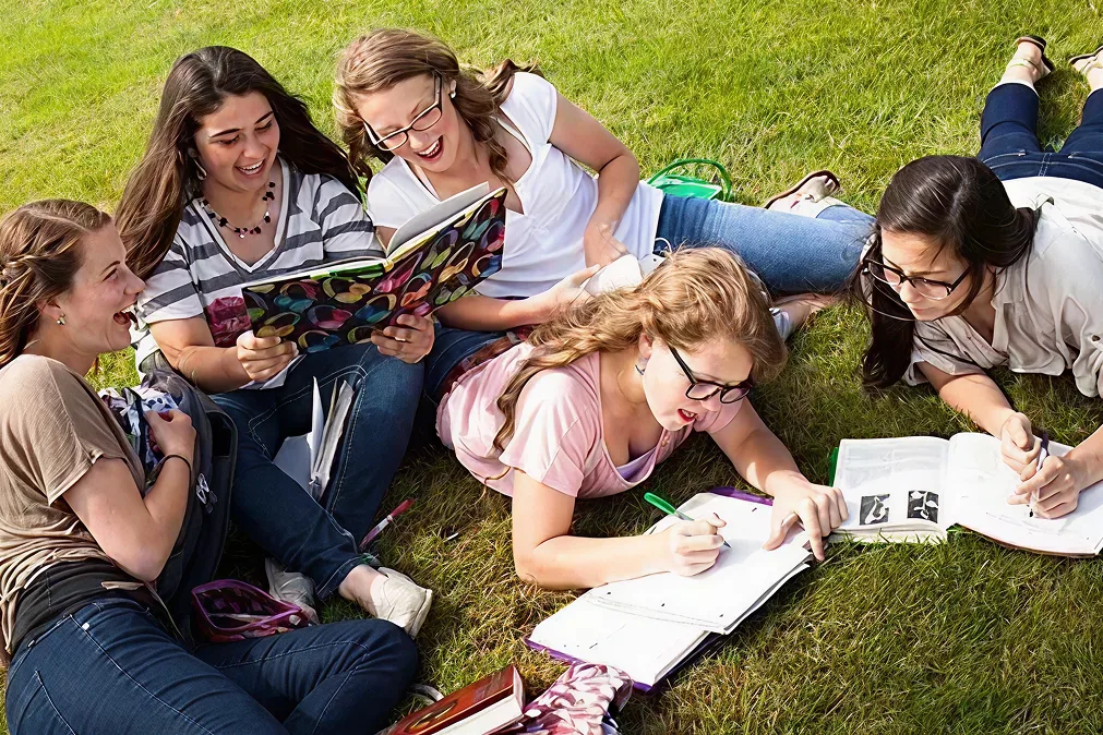 5 jeunes filles allongées sur l'herbe et font leurs devoirs