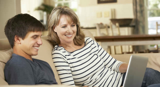 Maman et fils avec ordinateur portable sont assis sur un canapé