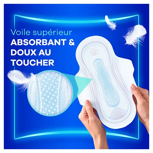 Mains tenant une serviette menstruelle avec ailettes Always Ultra avec une loupe montrant le voile supérieur absorbant et doux au toucher