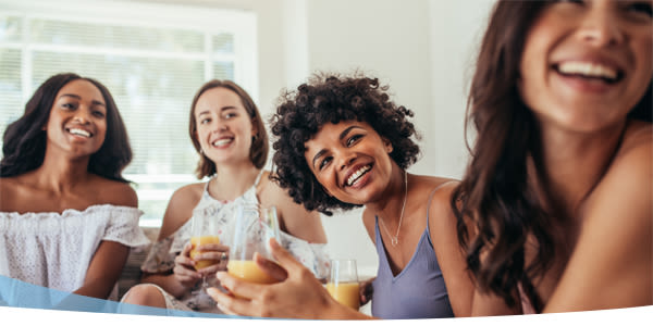 Quatre jeunes femmes souriantes buvant du jus d'orange