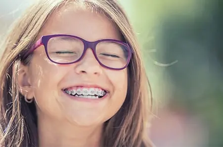 beépített fogszabályzós és szemüveges szőkésbarna hajú lány mosolyog