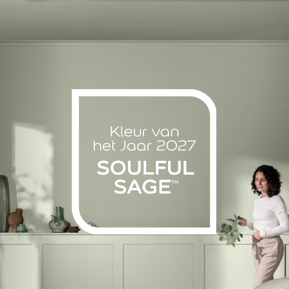 Moderne keuken met vrouw in wit shirt, tekst toont Kleur van het Jaar 2027 Soulful Sage op grijsgroene muur.