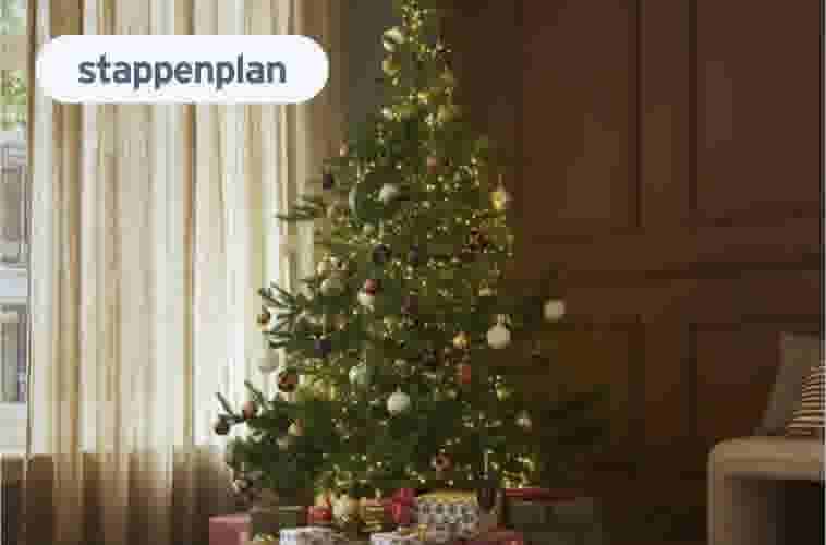 Versierde kerstboom met lichtjes en kleurrijke kerstballen in een woonkamer met beige gordijnen en cadeaus eronder.