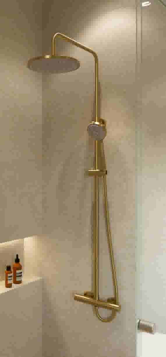 Gouden regendouche met handdouche tegen beige betegelde douchewand met glazen deur en toiletartikelen op plank