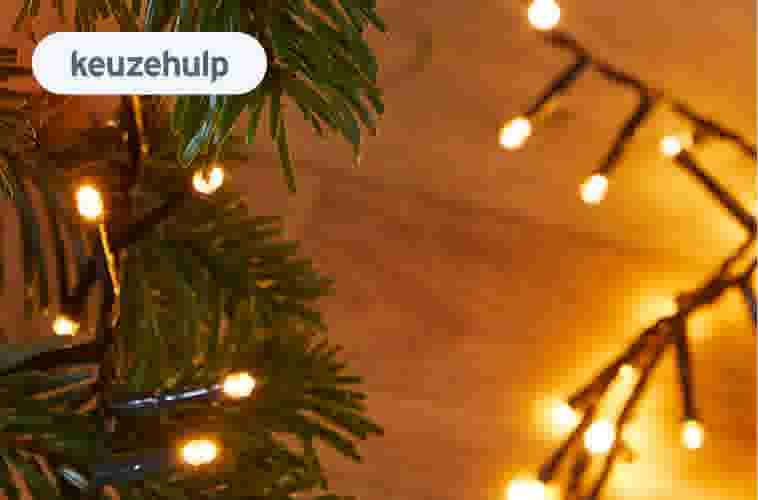 Groene kerstboomtakken met warme gouden kerstverlichting tegen een houten achtergrond met bokeh-effect.