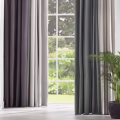 Gris et beige rideaux devant une grande fenêtre avec vue sur un jardin verdoyant. Une plante se trouve à droite.