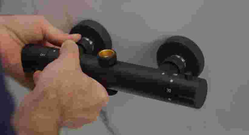 Hand stelt een zwarte thermostaatkraan in met twee draaiknoppen en een gouden aansluiting in het midden.