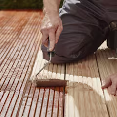 Homme appliquant de la lasure sur une terrasse