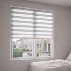 Wit en grijs duo rolgordijn voor een raam met uitzicht op een straat, in een lichte slaapkamer.