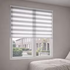 Grijze duorolgordijn half neergelaten voor een raam met uitzicht op een straat, in een lichte slaapkamer.