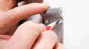 Hand gebruikt een kleine rode schroevendraaier om een metalen slot of schakelaar aan te passen.