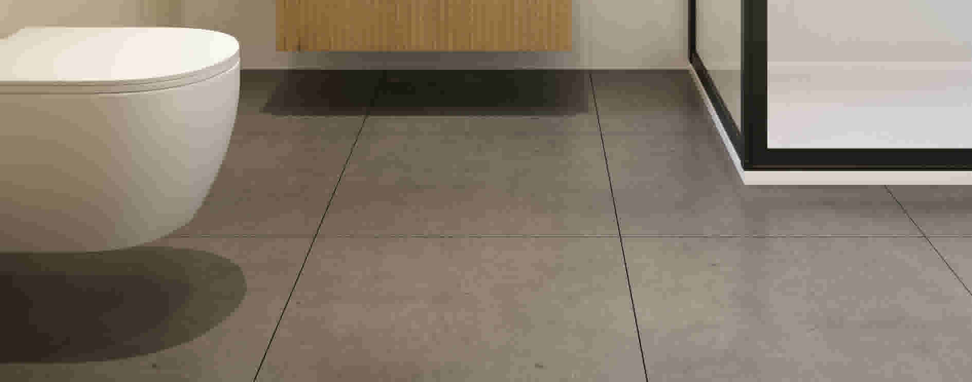 Moderne badkamer met grijze tegelvloer, wit toilet en houten kastje. Zwart frame van douchewand zichtbaar aan de rechterkant.