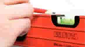 Hand houdt een oranje waterpas vast met een groene luchtbel die aangeeft dat het oppervlak waterpas is.