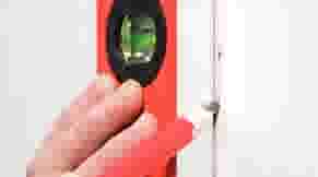 Een hand houdt een rode waterpas tegen een witte deurpost om te controleren of deze recht is.