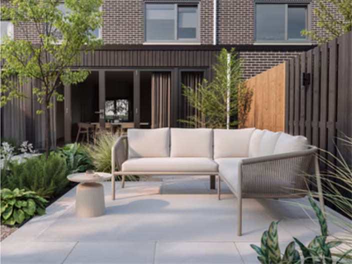 Modern terras met lichte hoekbank, groene planten en strakke bestrating voor een modern woonhuis met bakstenen gevel.