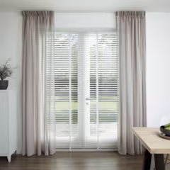 Lichte beige gordijnen voor een glazen deur met witte jaloezieen in een moderne woonkamer met houten tafel.