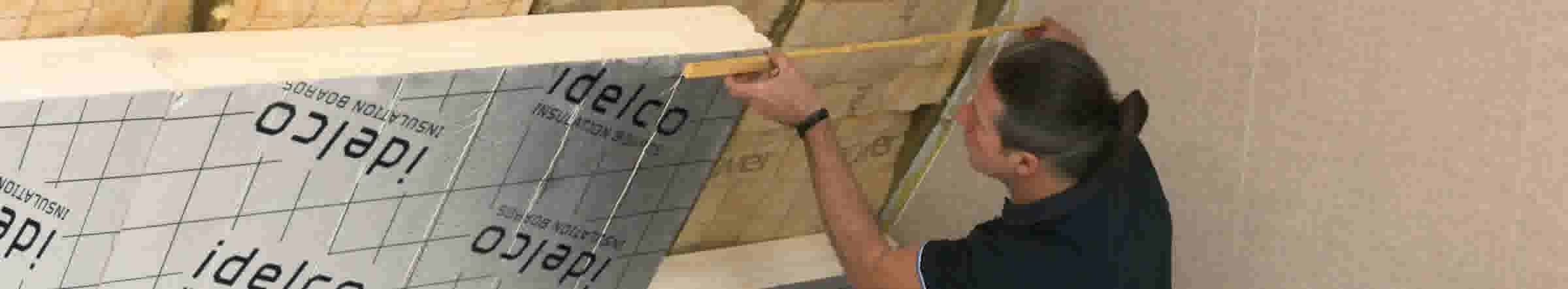 Ouvrier installant des panneaux d'isolation Idelco sur un mur en construction avec un mètre ruban jaune.