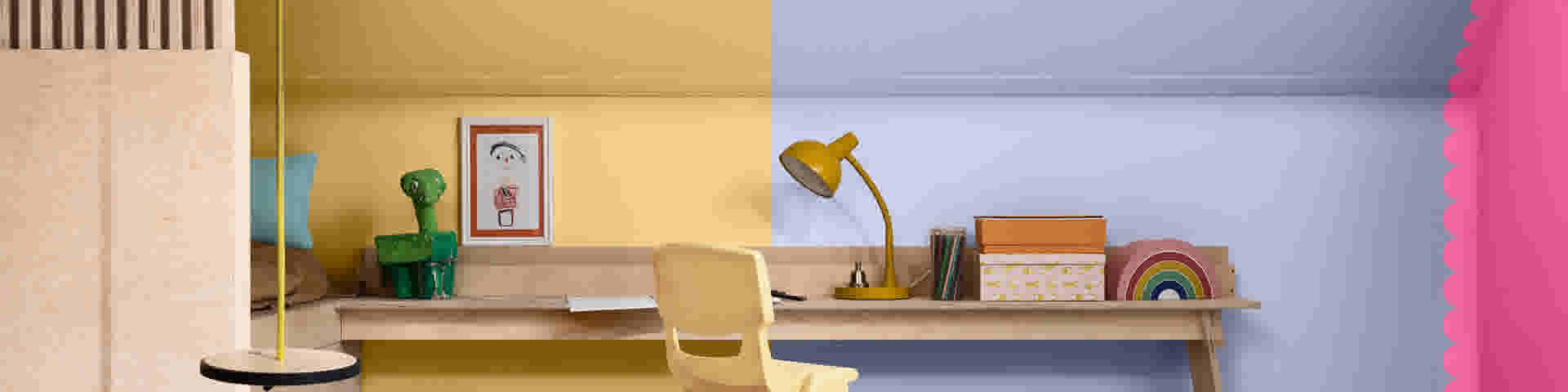 Kinderkamer met houten bureau, gele lamp en speelgoed. Muur is half geel, half lichtblauw geschilderd.