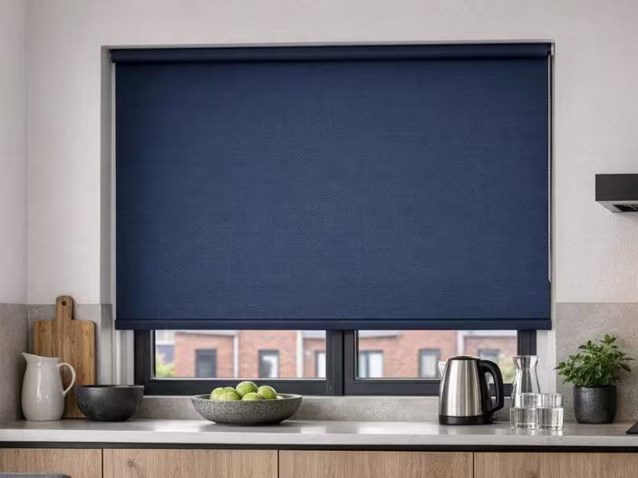 Donkerblauwe rolgordijn voor keukenraam, met aanrecht, waterkoker, kom met appels en snijplank.