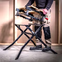 Un établi Workmate est posé au sol, et un homme en retire la partie supérieure