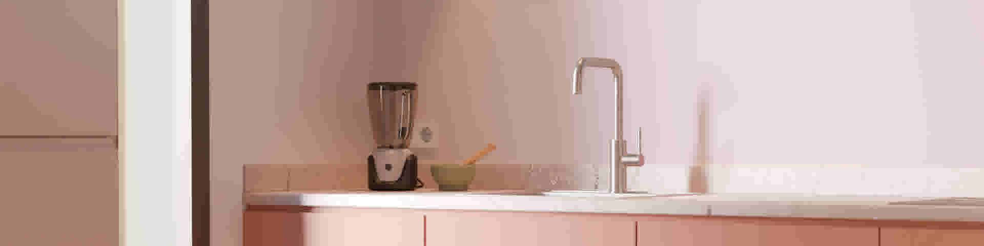 Roze keuken met marmeren aanrecht, een blender, groene vijzel met stamper en een zilveren kraan boven de gootsteen.