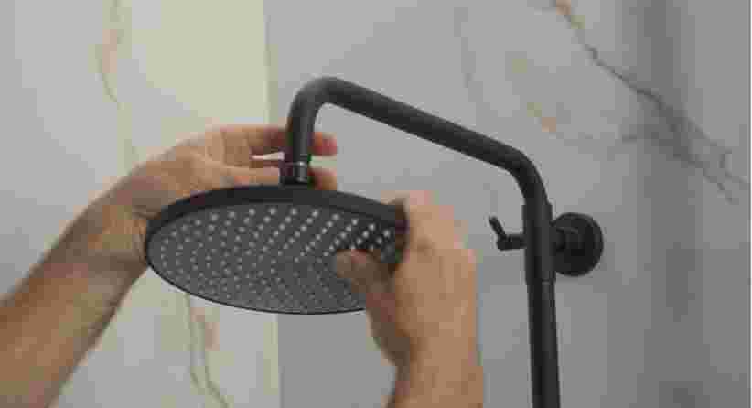 Handen installeren een ronde zwarte douchekop op een matzwarte douchearm tegen een marmeren badkamerwand.