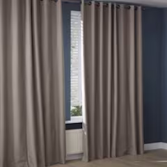 Beige gordijnen met ringen hangen voor een raam in een kamer met donkerblauwe muren, met een radiator eronder zichtbaar.