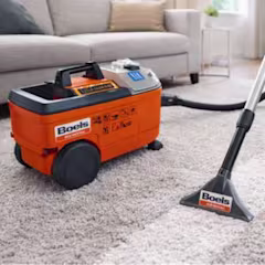 Oranje gehuurde tapijtreiniger van RentPartner Boels op een lichtgekleurd tapijt in een woonkamer, met stofzuigerslang klaar voor gebruik.