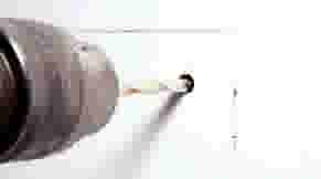 Een boormachine met een boor die een gat maakt in een witte muur, met markeringen voor extra boorgaten.