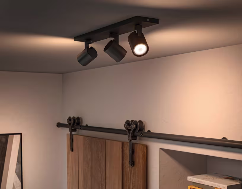 Moderne zwarte plafondspot met drie verstelbare lampen, waarvan één verlicht, boven houten schuifdeuren.