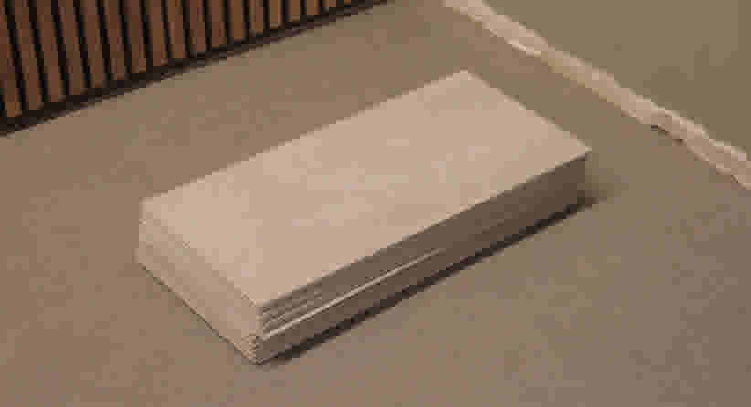 Stapel lichtbeige clickvinyl op een grijze vloer, naast een muur met lattenwand