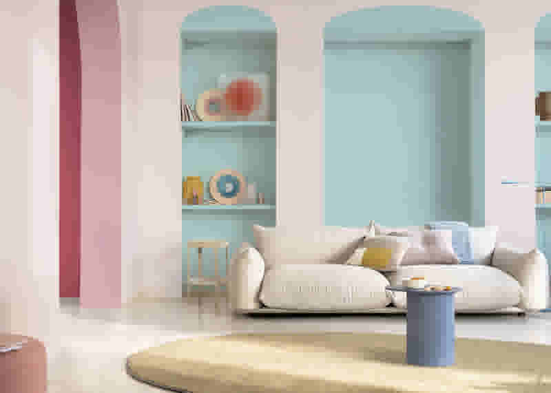 Lichte woonkamer met roze en mintgroene bogen, een beige bank met kussens, ronde vloerkleed en blauwe salontafel.