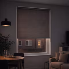 Store enrouleur marron foncé à moitié baissé sur une fenêtre, dans un salon sombre et cosy le soir.