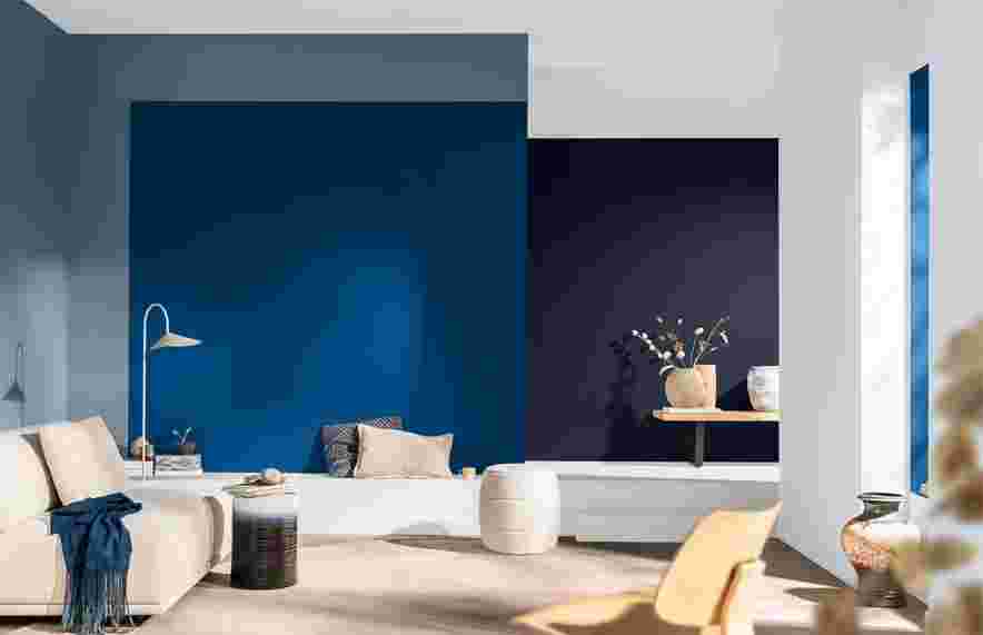 Modern woonkamer met contrasterende blauwe en donkere muren, lichte bank, houten bijzettafel en decoratieve vazen met takjes.