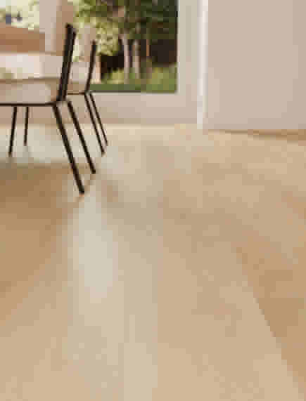 Parquet en bois clair avec chaises noires à pieds fins, près d'une fenêtre donnant sur un jardin verdoyant.