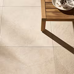 Beige tegelvloer met een houten tafel en een witte kom met noten, gefotografeerd in zonlicht.