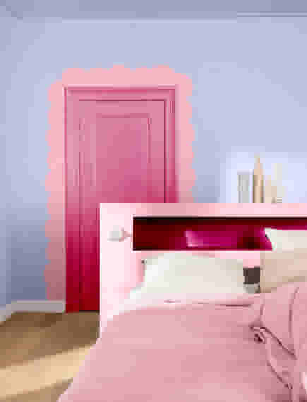 Slaapkamer met lichtblauwe muren, roze bed en hoofdbord, en een felroze deur met golvend roze kader eromheen.