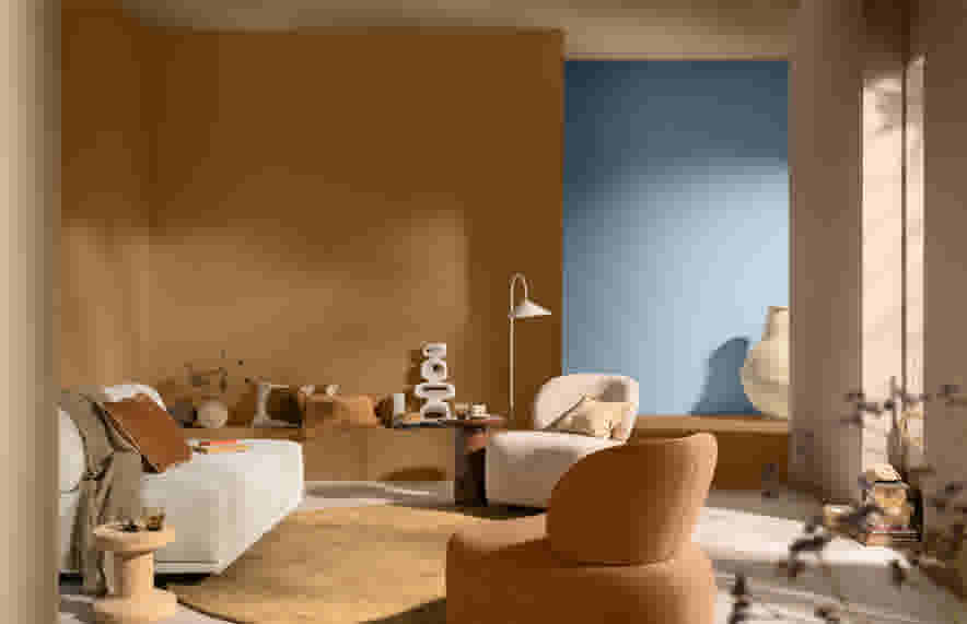 Salon moderne avec murs terracotta et bleu, canapé blanc, fauteuils beiges et décorations minimalistes sur un tapis rond.