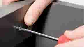 Een hand gebruikt een kleine schroevendraaier om een schroef in een zwart apparaat vast te draaien.