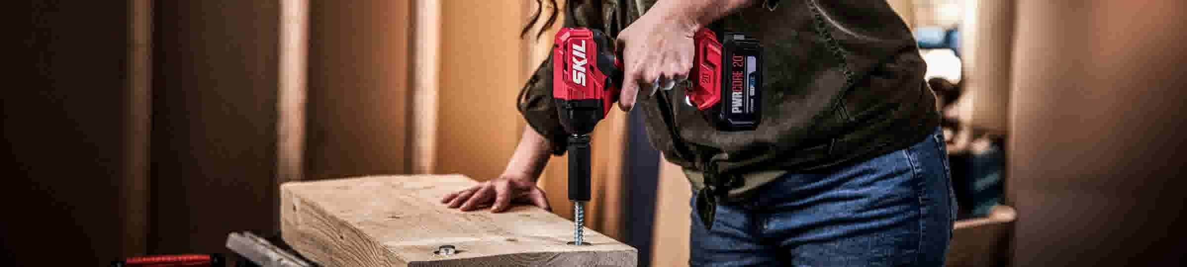 Personne utilisant une perceuse-visseuse sans fil rouge SKIL avec batterie pour visser dans une planche de bois.