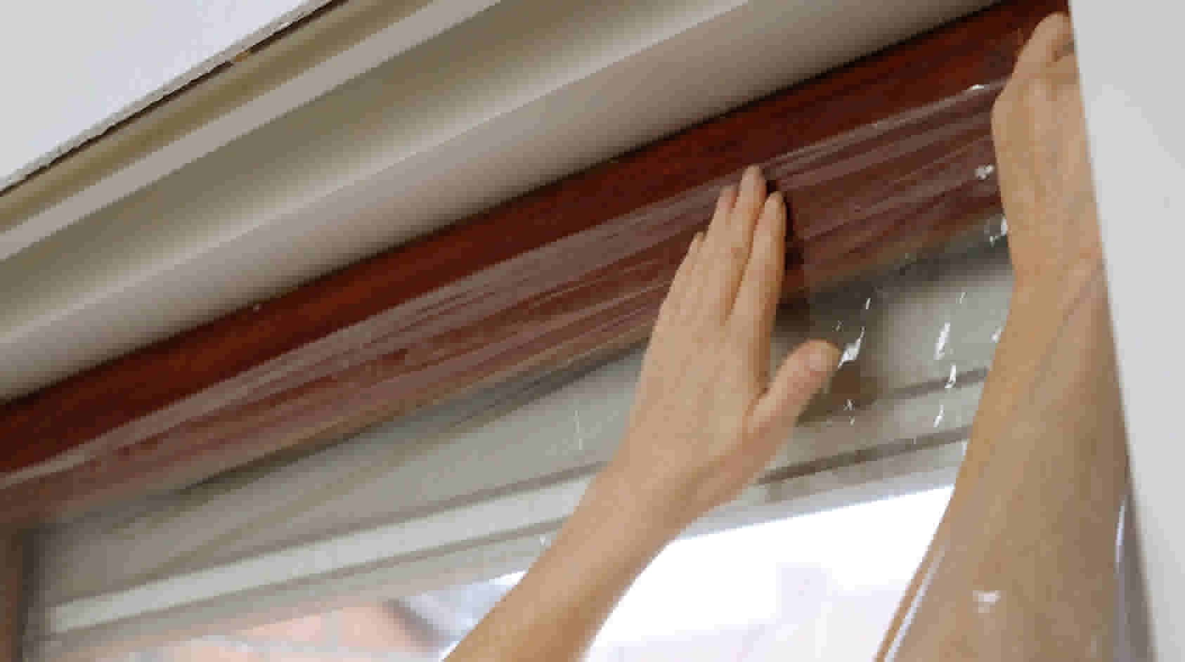 Handen plaatsen doorzichtig isolatiefolie op raam met houten kozijn om tocht en warmteverlies tegen te gaan.