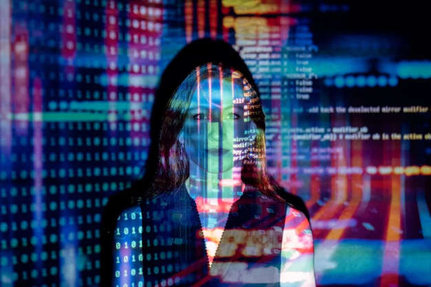 A woman stands in front of a projection screen with data and code displayed on her face and the screen behind.