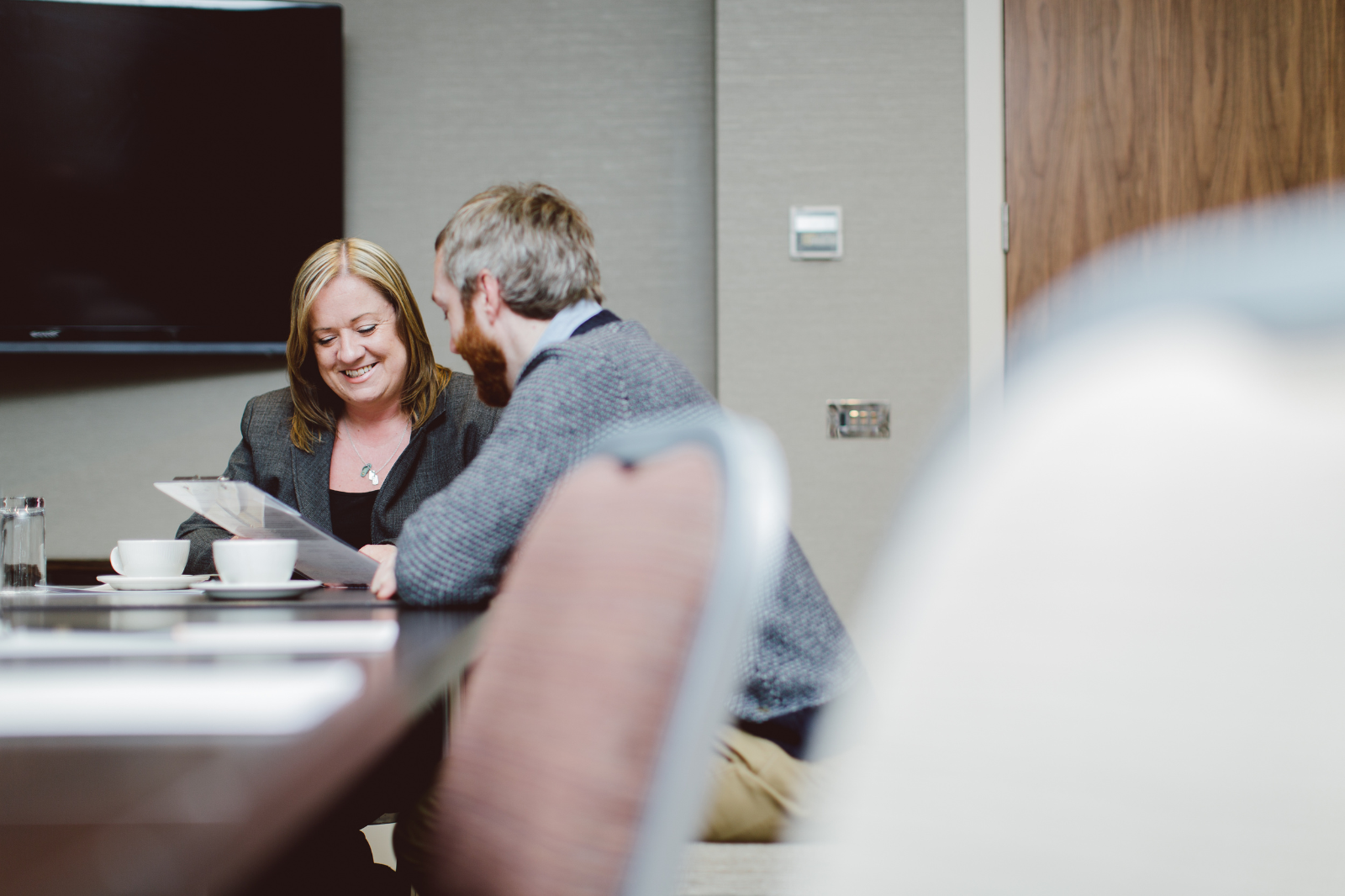 Two professional individuals sit in a conference room in discussion. 