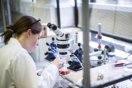 Female scientist in lab suit examining pathogens through a microscope.