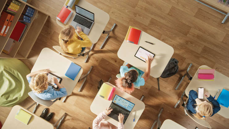 hildren Sitting at their School Desk Using Personal Computers and Digital Tablets for Assignments. - stock photo